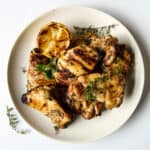 Grilled Boneless Chicken Thighs piled on a white plate garnished with thyme.