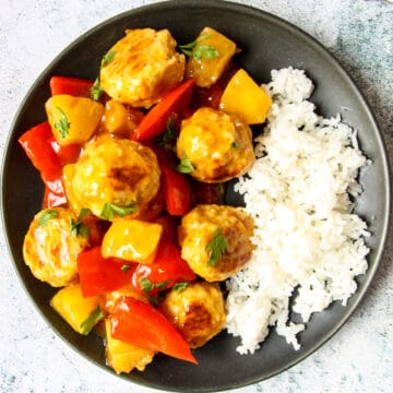 A serving of sweet and sour meatballs alongside white rice on a black plate.