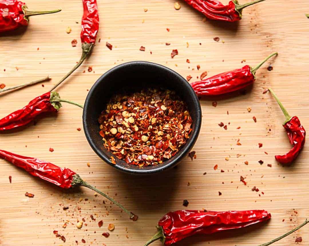 A dish of crushed dried chile peppers and whole chiles on a wooden table