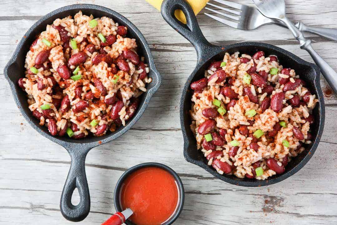 Two small black skillets filled with rice and beans on wooden table.
