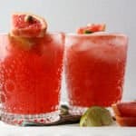 Two glasses filled with pink liquid and ice