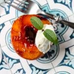 A spiced rum grilled peach on a blue and white plate topped with ice cream.
