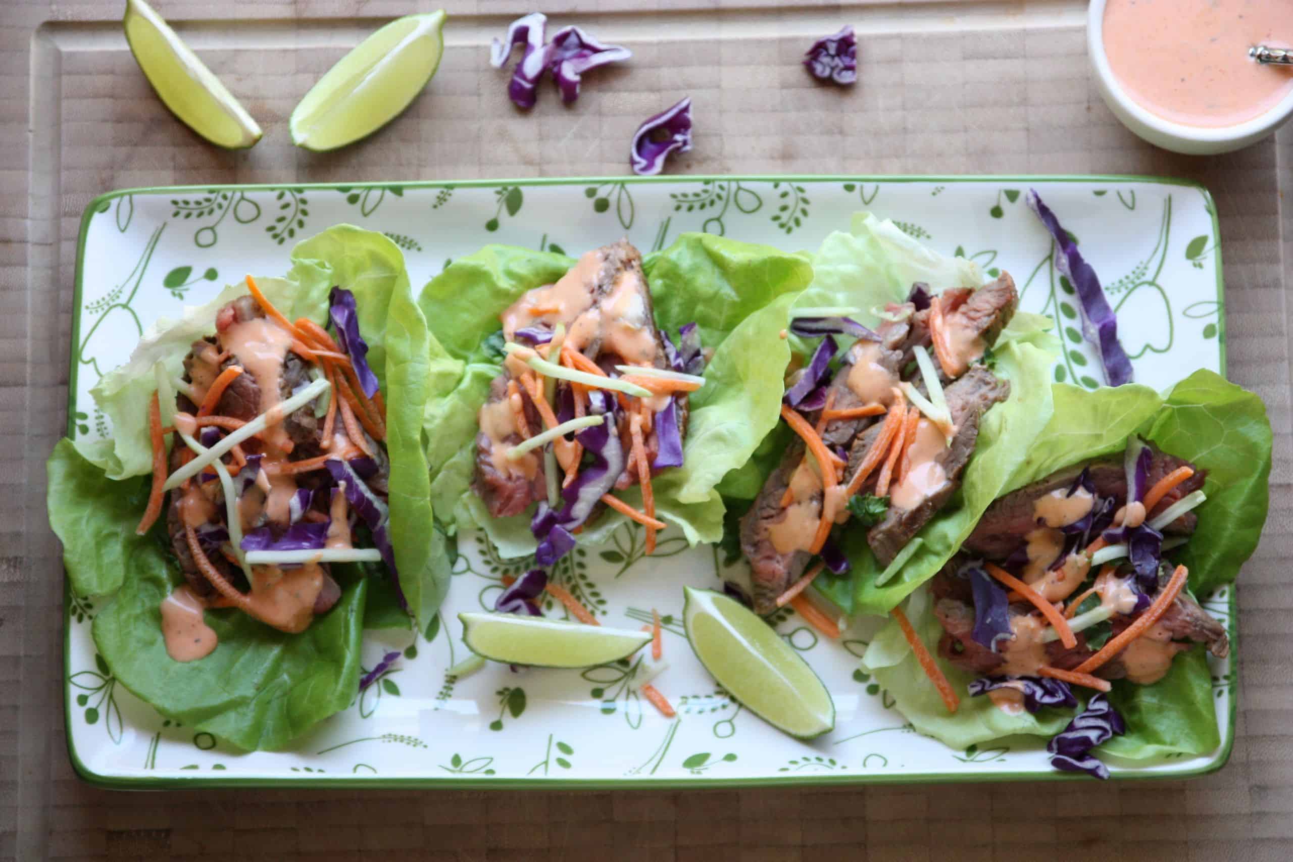 four steak lettuce wraps on a green and white platter with lime wedges