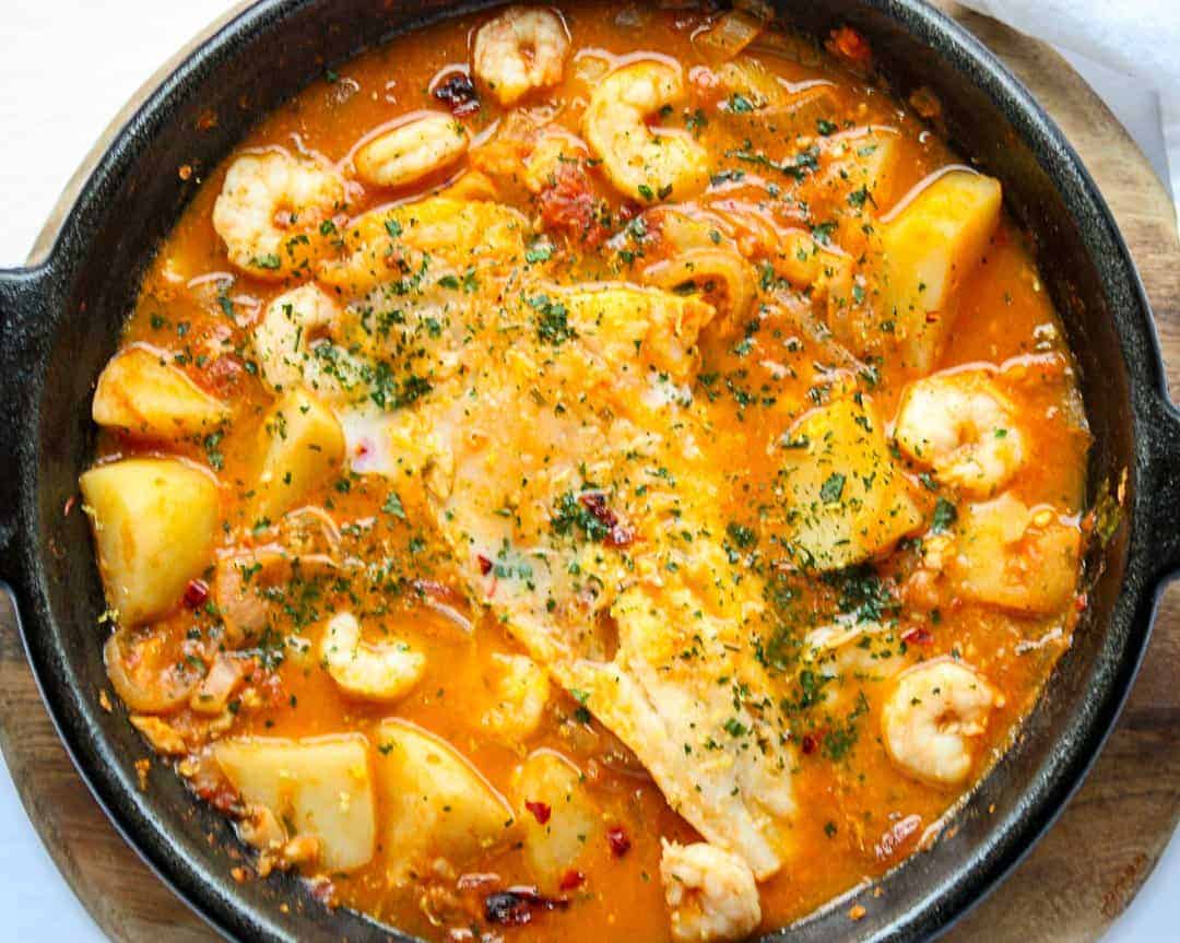 Spanish fish stew cooking in a cast iron skillet with shrimp, cod, and potatoes in a tomato broth