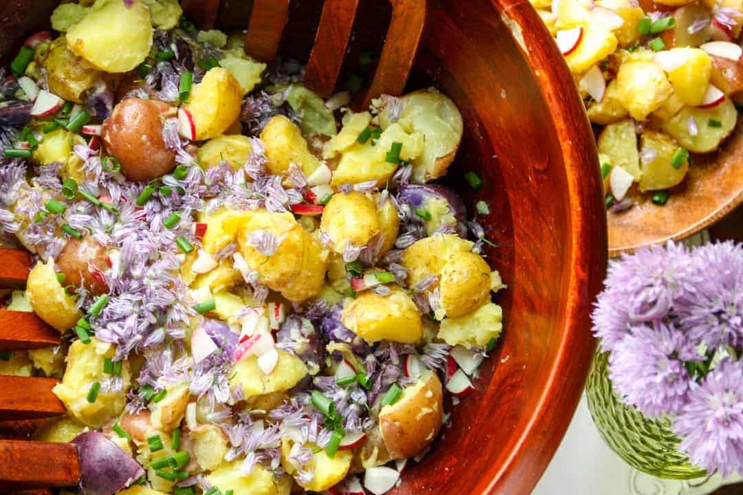 Wooden salad bowl with new potato, chive blossom, and spring radish