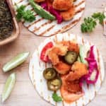 Coconut Shrimp Tacos with lime wedges on a cutting board.