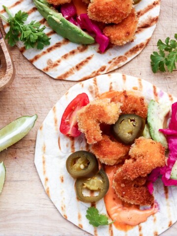 Coconut Shrimp Tacos with lime wedges on a cutting board.