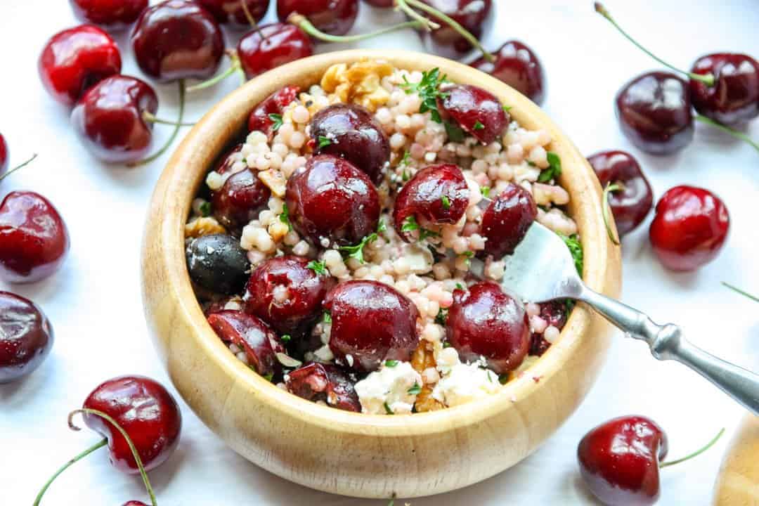 A bowl of salad with cherries and a fork