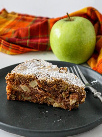 A slice of apple walnut cake on a black plate.