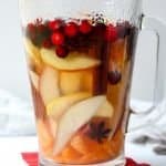 A close up of a glass jug on a table, with Sangria and fruit
