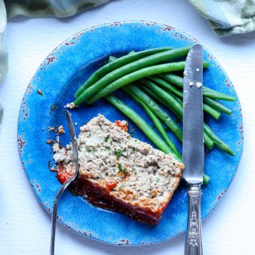 A piece of meatloaf  on a plate with a fork and knife