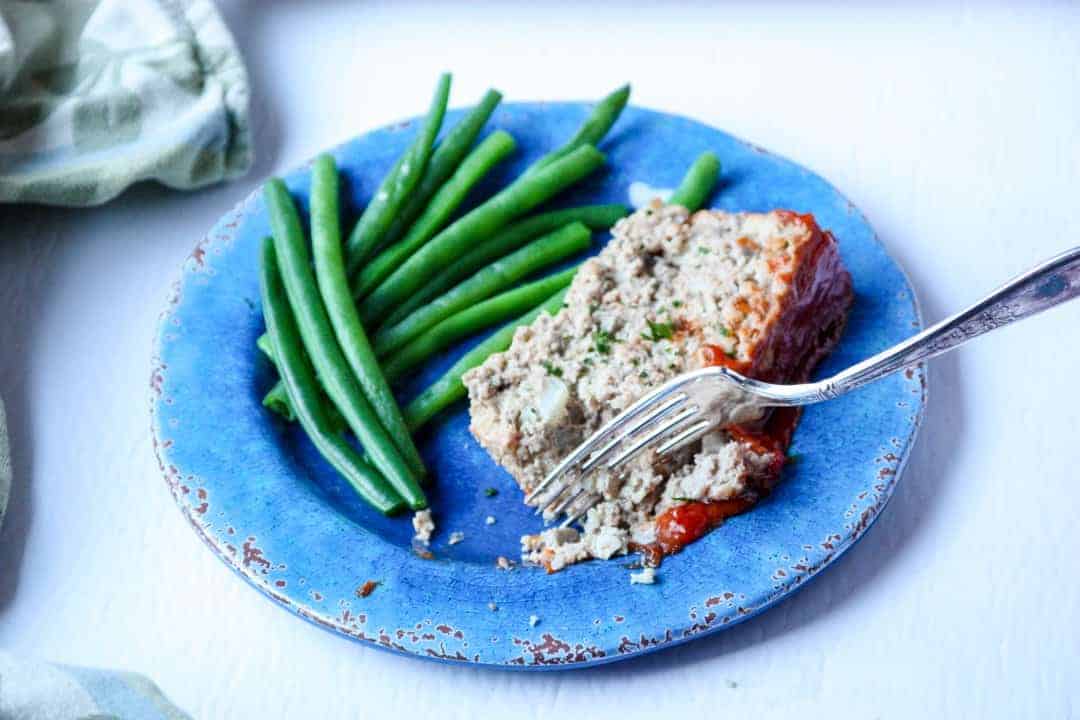 Meatloaf and green beans on a plate with a fork