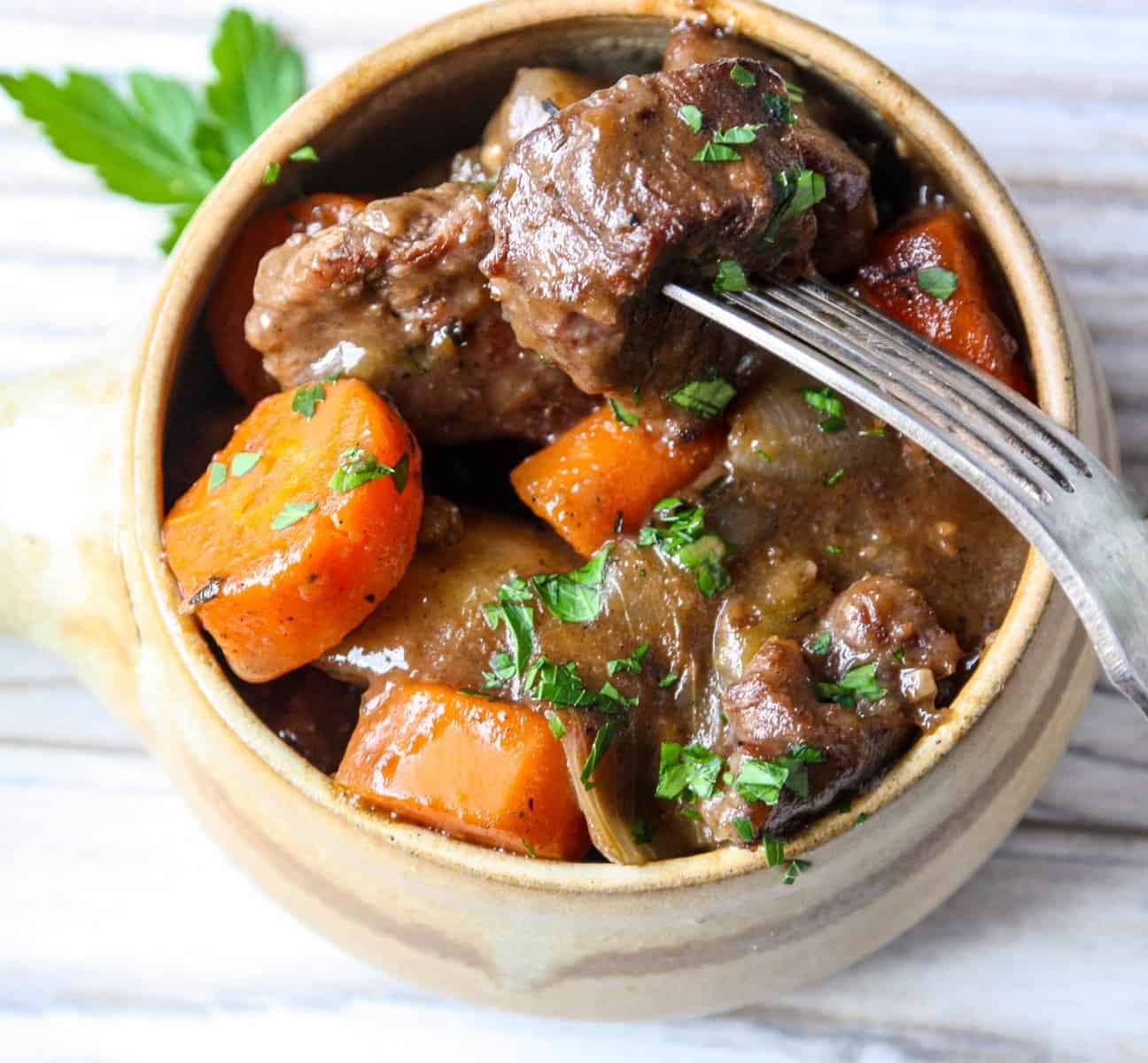 A bowl of stew with beef and carrots in gravy.
