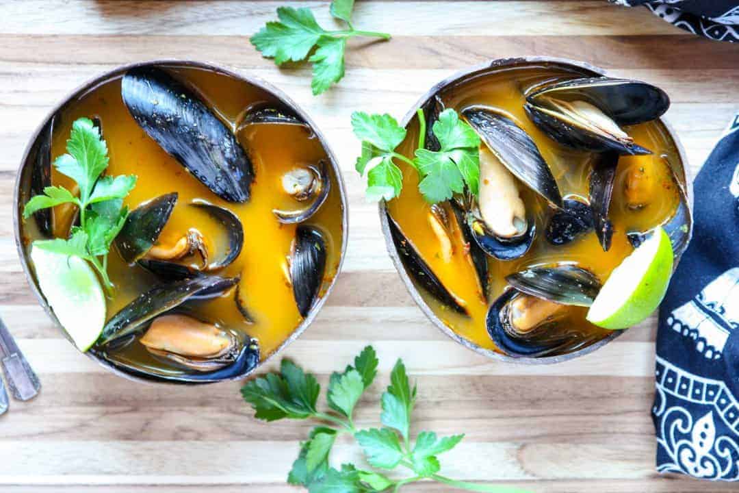 Mussels in orange broth in brown wooden bowl on wooden table