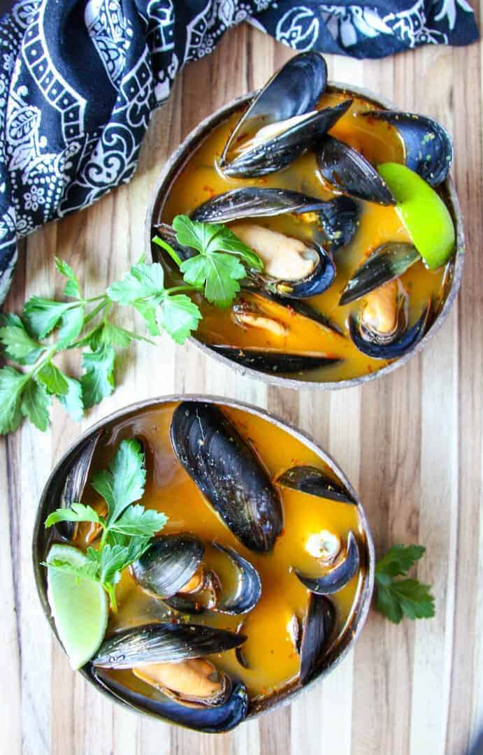 Mussels in orange broth in brown wooden bowl on wooden table