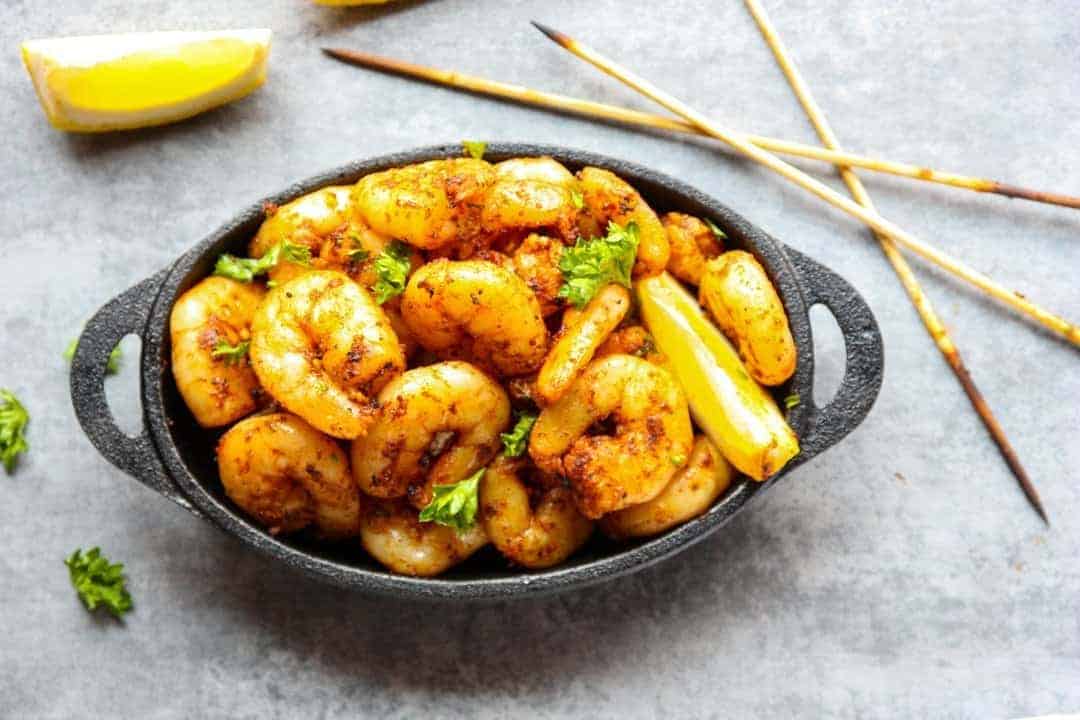 A close up of a pan of cooked shrimp on a table, with lemon wedges