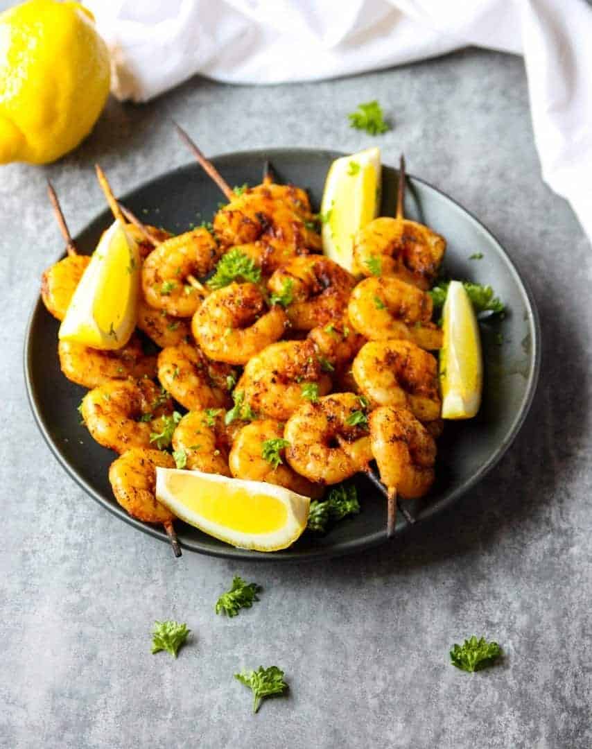 The skewers on a black plate with lemon wedges.