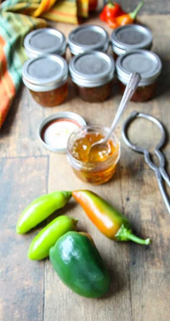 A jar of pepper jelly with a spoon in it, with peppers