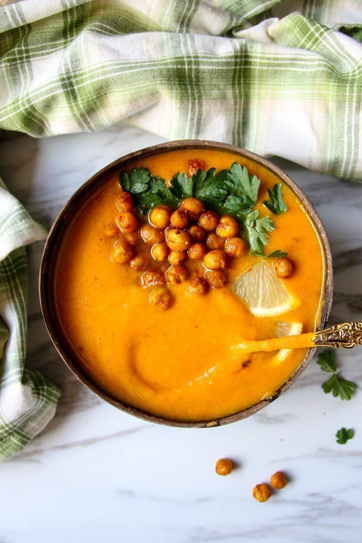 Sweet potato soup in a coconut shell bowl, topped with roasted chickpeas and parsley