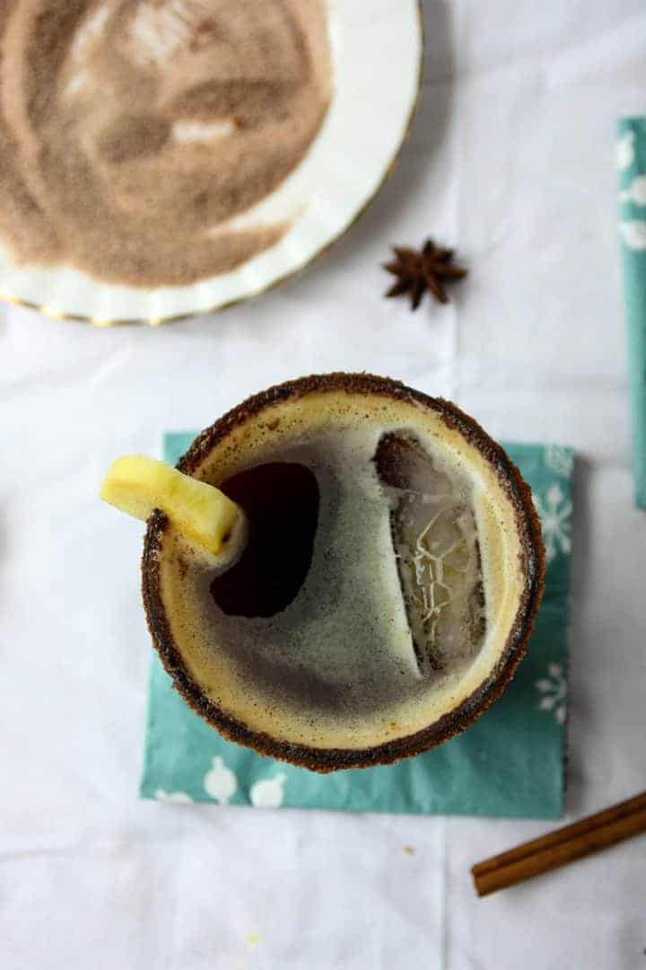 Cocktail in a glass on blue napkin next to cinnamon sugar on a round white plate