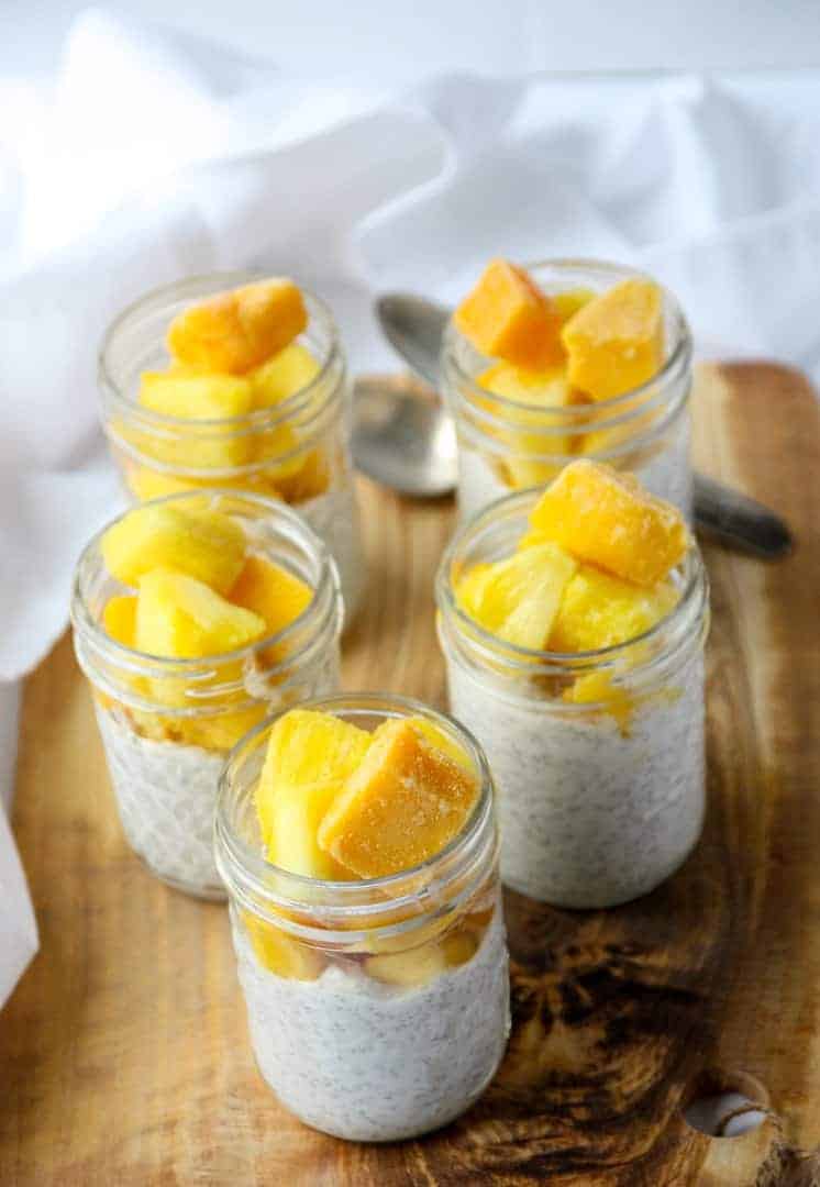Five half pint jars of chia pudding topped with mango and pineapple