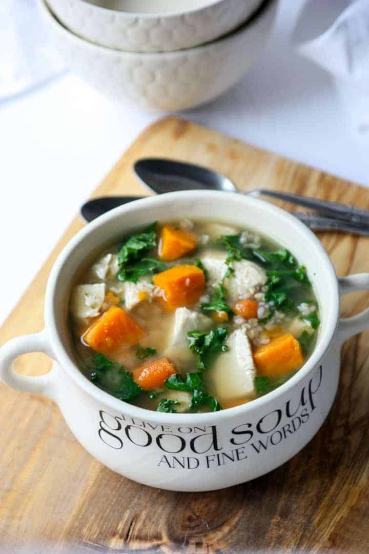 Buckwheat Soup with turkey, sweet potatoes and kale in a white bowl on a wood cutting board.