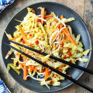 Cabbage stir fry on a black plate with black chopsticks