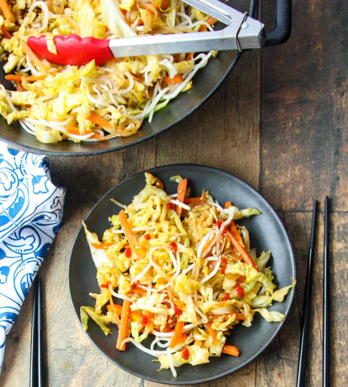 Cabbage stir fry being served from a wok onto a black plate, using tongs.