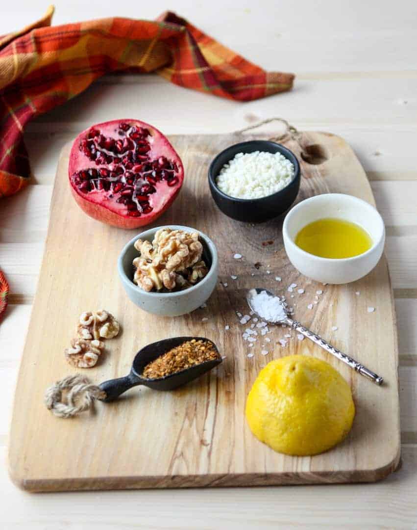 Ingredients for Muhammara on a wooden board includin lemon, walnuts, breadcrumbs and pomegranate
