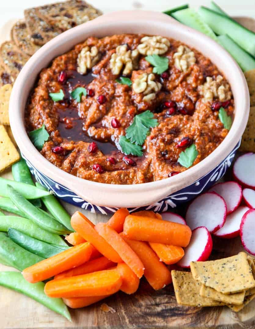 Muhammara dip in a clay bowl with dipping vegetables and crackers