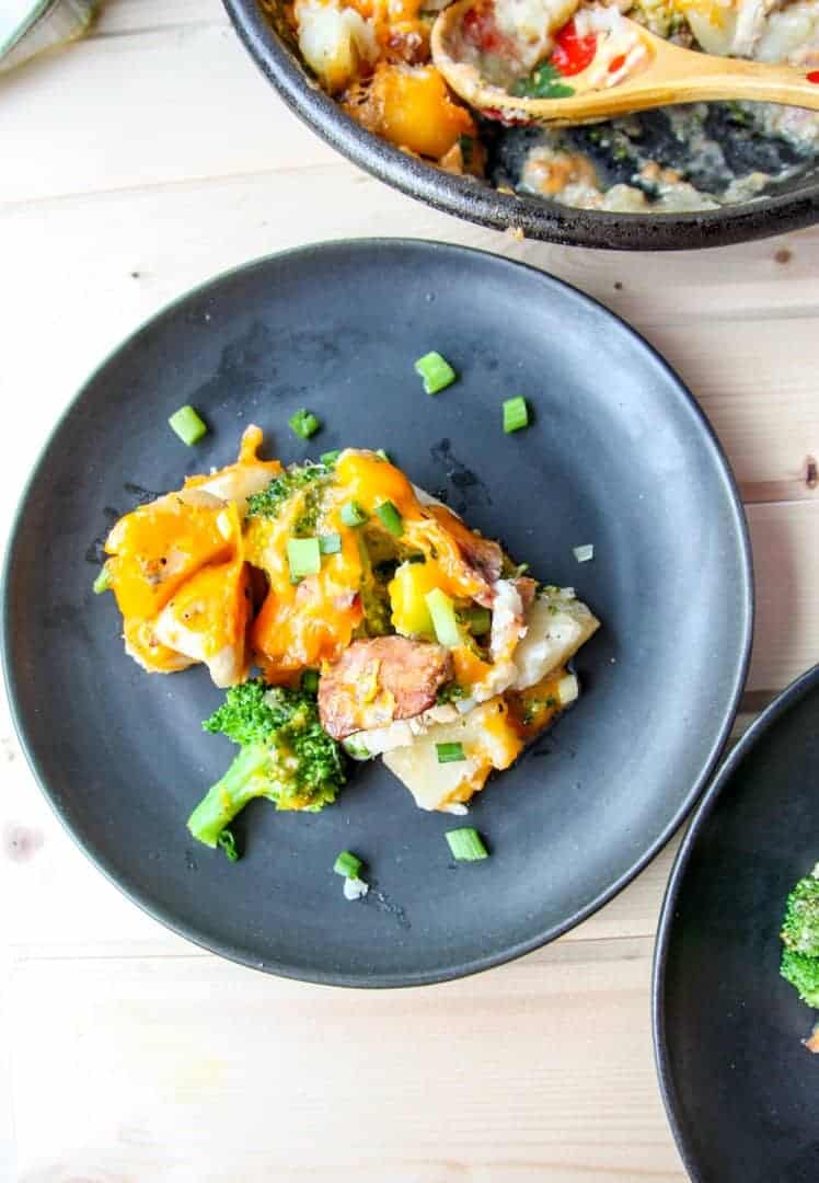 A black plate with cheese, broccoli and potatoes on top.