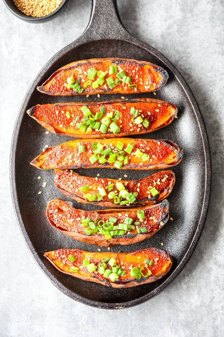 Six miso baked sweet potato halves on a black cast iron skillet.