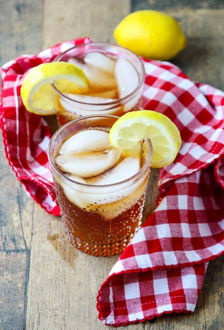 two glasses of spiked liced tea with ice cubes and lemon slices