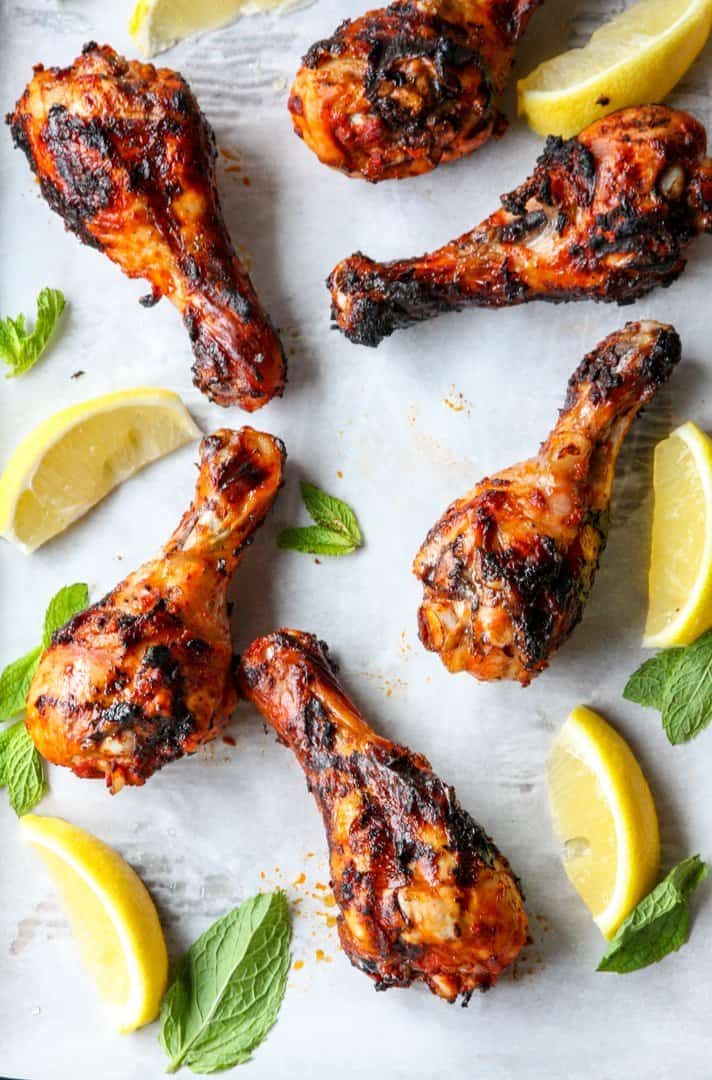 Six grilled harissa chicken drumsticks and lime wedges on parchment paper