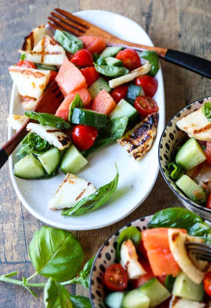 A bowl of fruit and vegetable salad on a plate, with Halloumi and Garnish