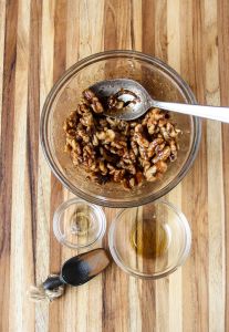 Ingredients for maple roasted walnuts being stirred together in a glass bowl.