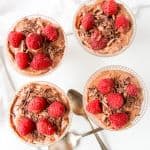 Top down view of four dishes of chocolate mousse topped with raspberries.