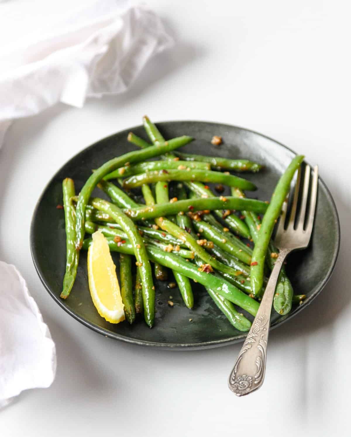 Sautéed green beans on a black plate with a silver fork.