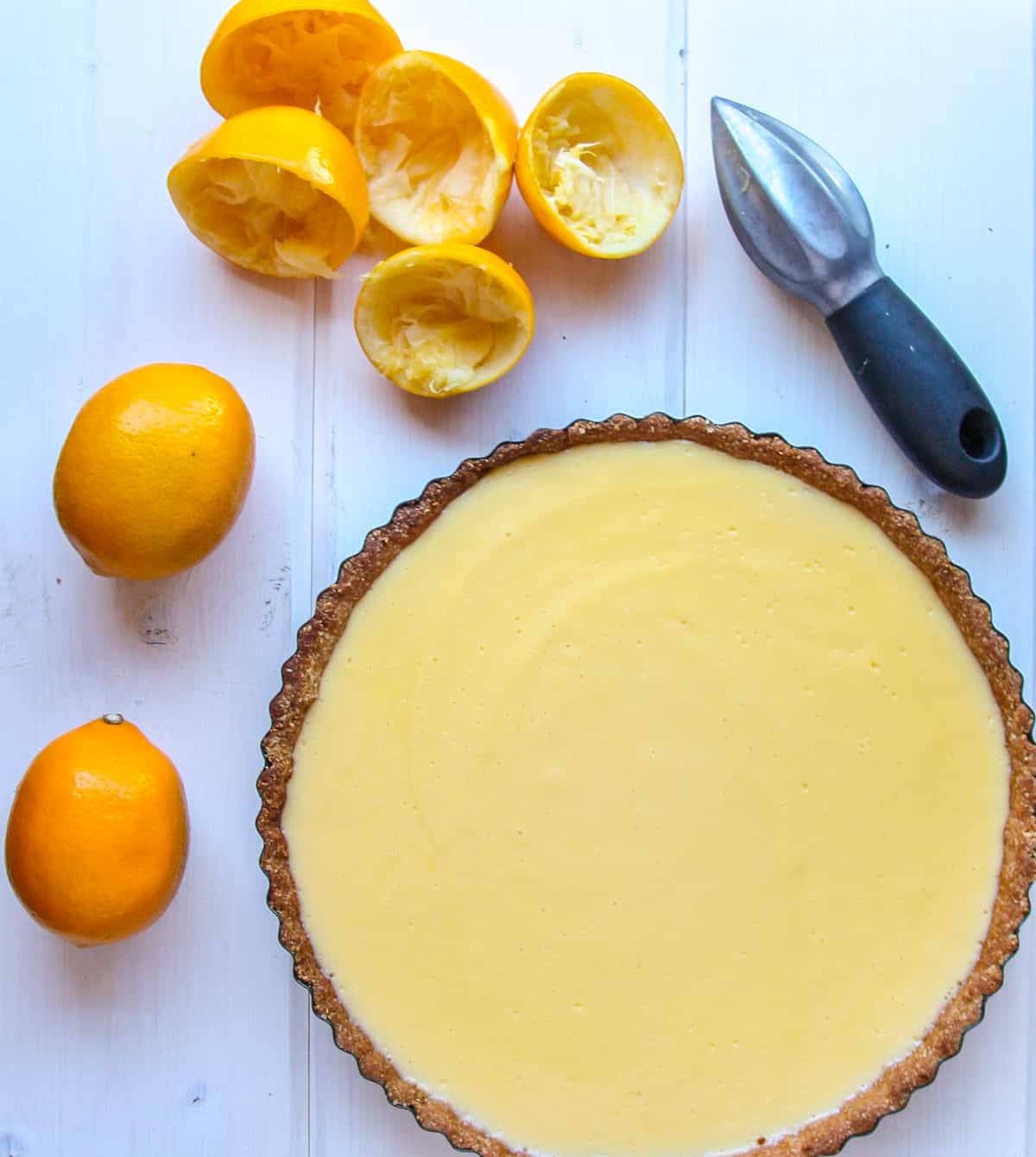 A Lemon Curd Tart on a table beside two lemons.