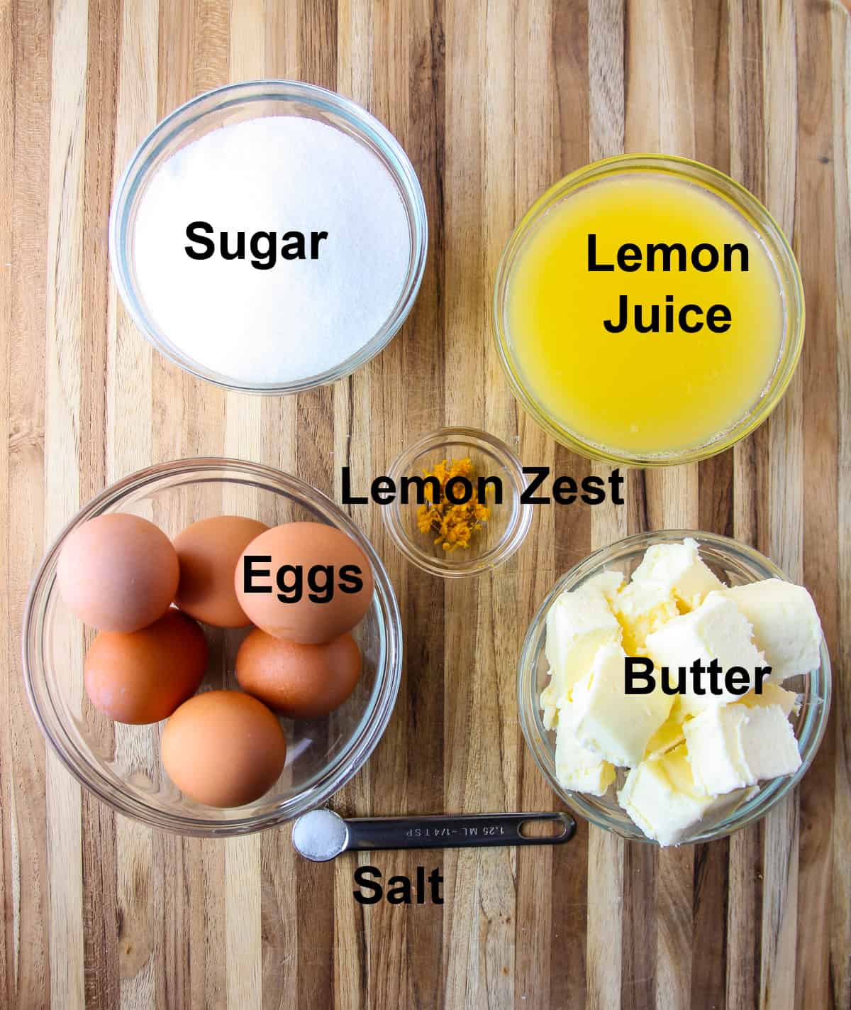 Ingredients to make meyer lemon curd filling in glass bowls on a wooden board.