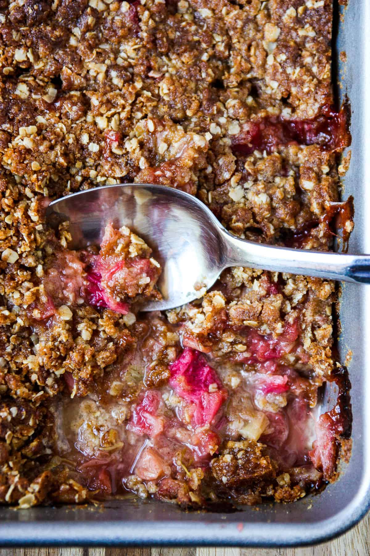A freshly baked pan of rhubarb crisp with a spoon in it.