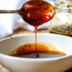 A spoon dripping with honey teriyaki sauce hovering over a white dish.