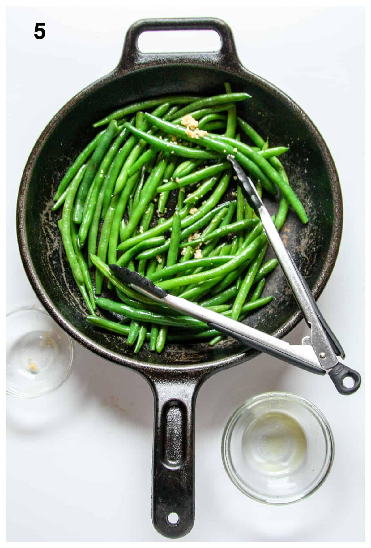 Garlic and seasonings being added to green beans in a cast iron pan.