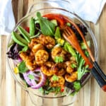Grilled shrimp salad in a glass bowl with two wooden forks.
