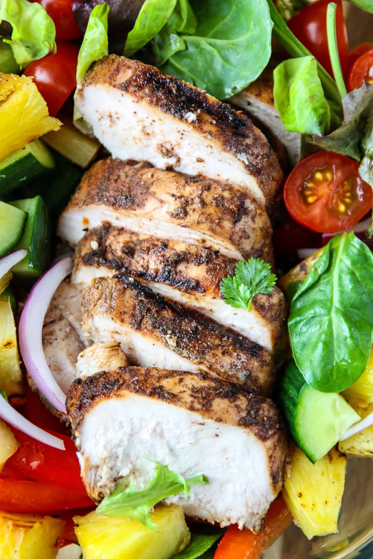 Slices of Grilled Jerk Chicken on a bed of greens.
