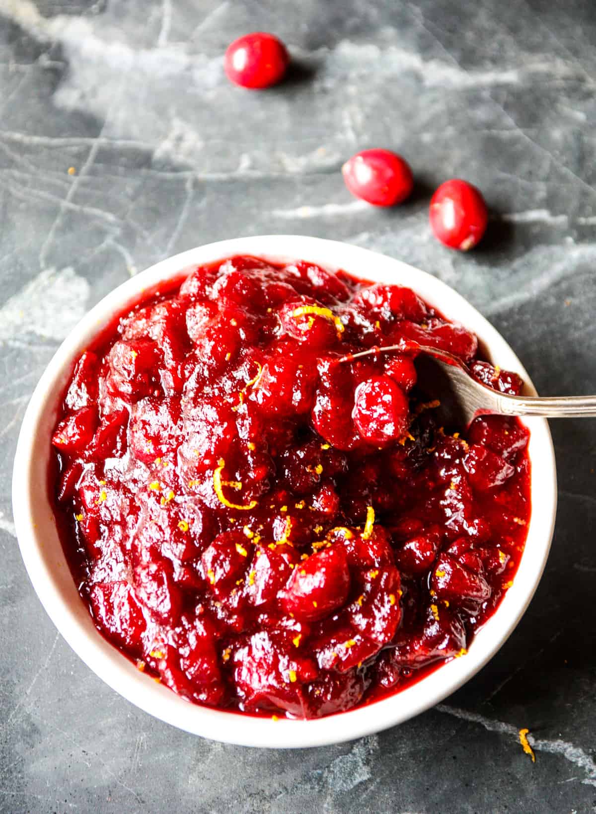 A serving spoon being dipped into a bowl of cranberry sauce.