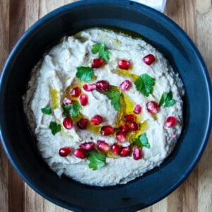 Mutabbal dip in a black dish, garnished with parsley and pomegranate seeds.