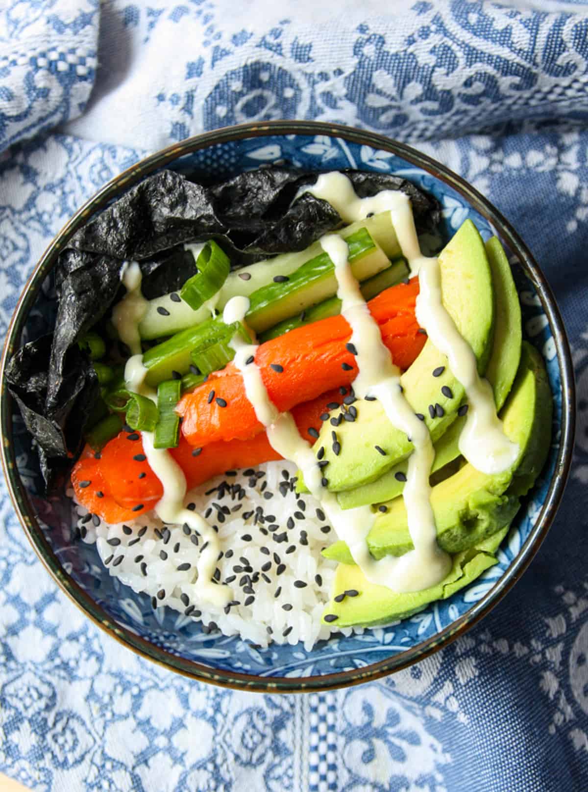 A sushi bowl with salmon, cucumber, avocado and seaweed.
