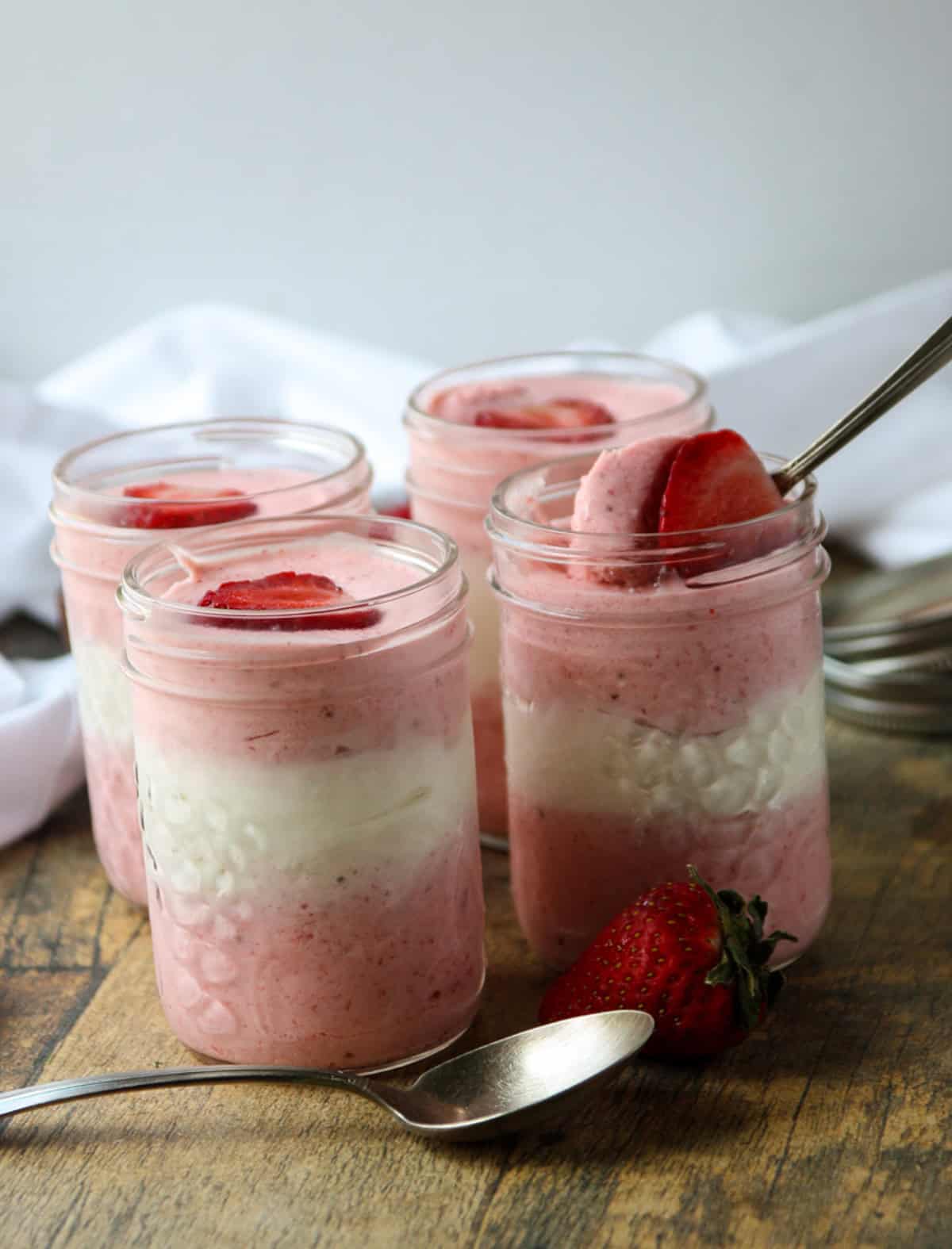 Four jars of pink and white  layered mousse topped with strawberries.