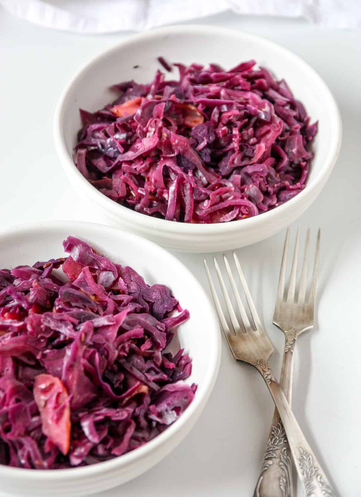 Braised red cabbage in two white bowls with two silver forks.